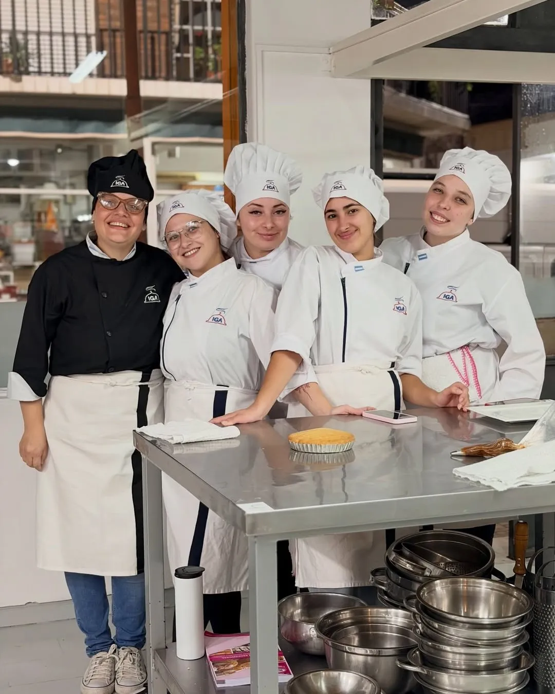 Alumnas y docente posando detrás de la mesada en una clase de pastelería