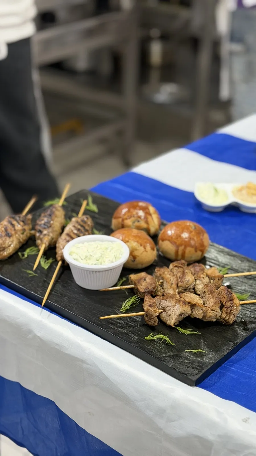 Brochetas y panes brioche sobre mesa con mantel azul