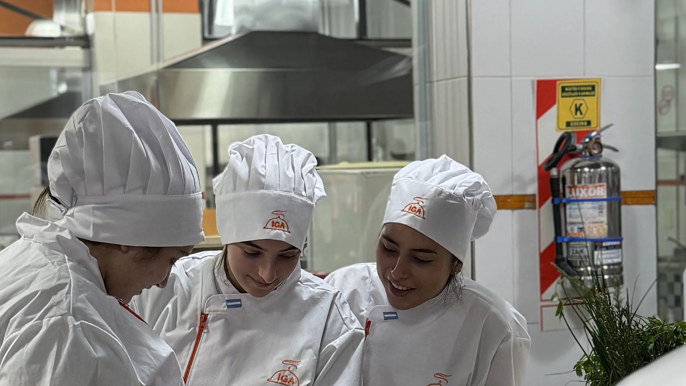 Tres alumnas con cofia de IGA trabajando juntas en la cocina